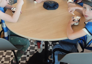 Wszystkie dzieci siedzą przy stolikach i jedzą lody