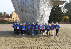 Dzieci w niebieskich kamizelkach przed Pomnikiem przy Muzeum.
