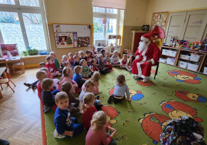 Dzieci siedzą obok Mikołaja i paczek świątecznych
