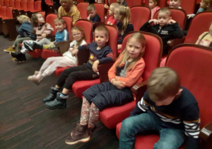 Dzieci siedzą na krzesłach w teatrze i czekają na spektakl