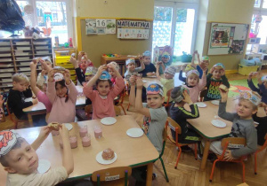 Dzieci zadowolone że mogą zjeść pączka na drugie śniadanie siedzą przy stolikach z opaskami na głowie.